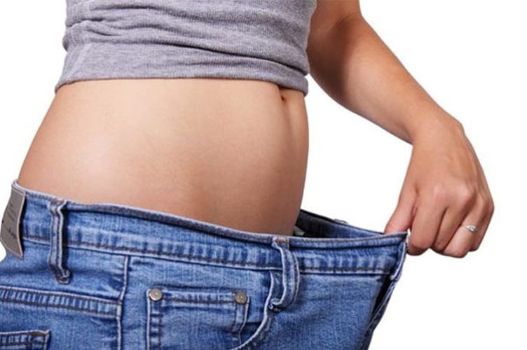 Woman pulling her jeans away from her abdomen to display fat loss