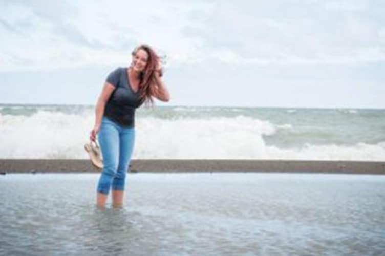 Woman standing in a lake or ocean holding flip flops and smiling for the camera