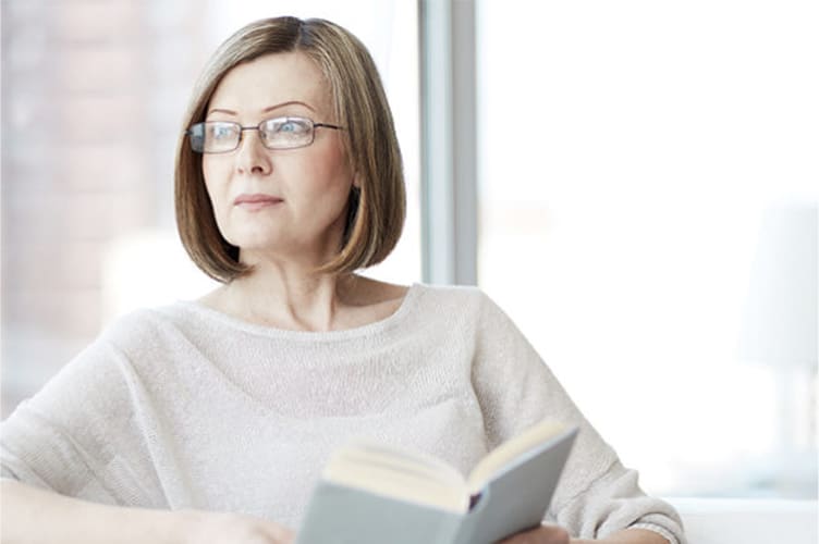 Woman wearing glasses looking off into the distance while reading a book