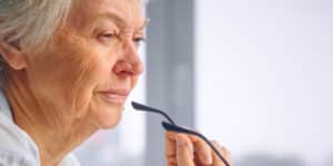 Older woman holding her glasses away from her face looking off into the distance