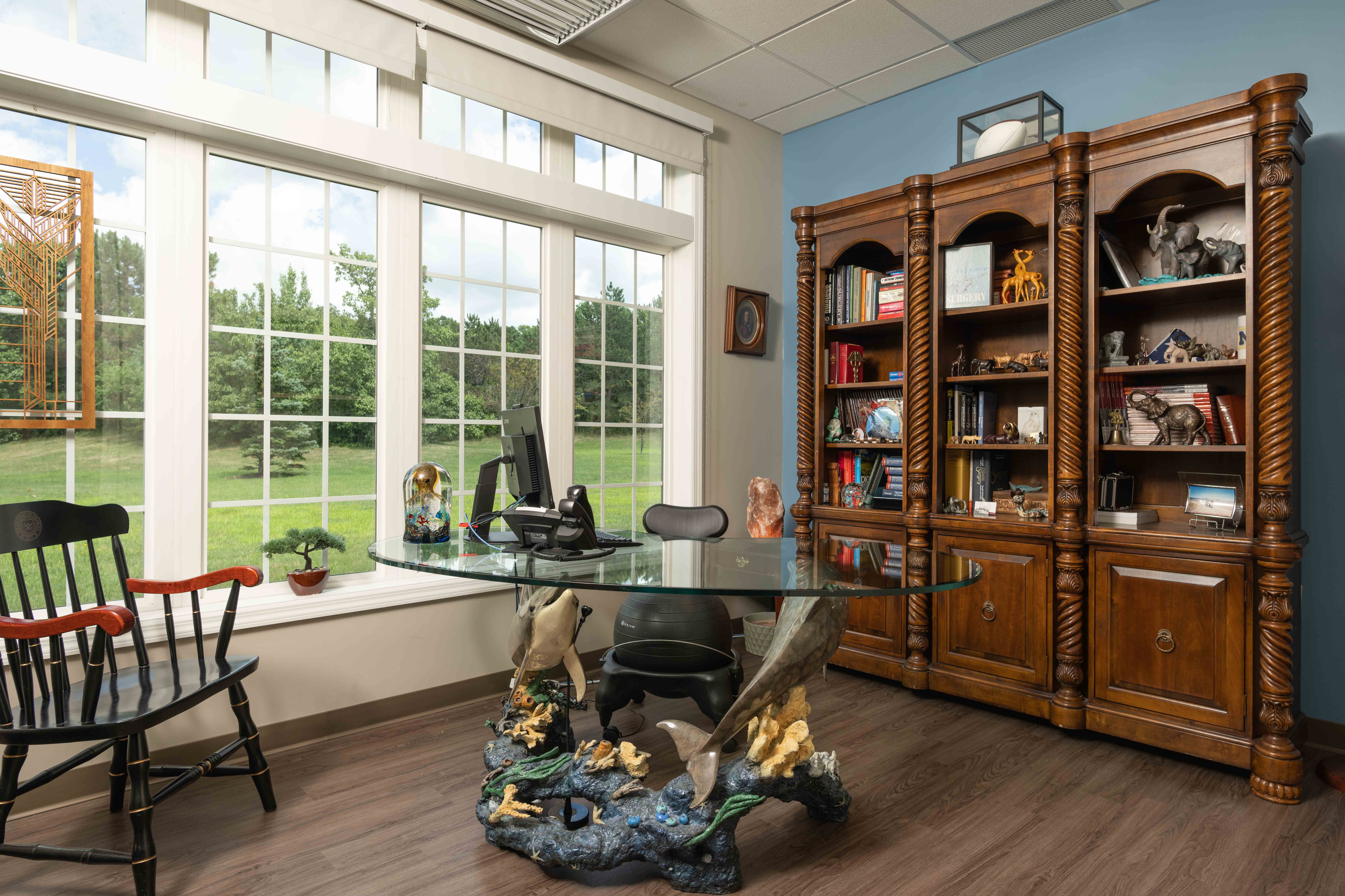 Office with an ocean-themed desk, large bay windows, and a bookshelf with elephant trinkets