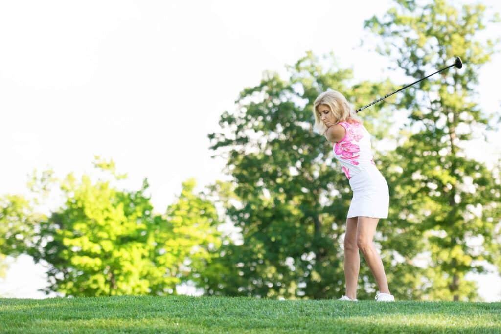 Carla in a pink golf top hitting a golf ball at the range