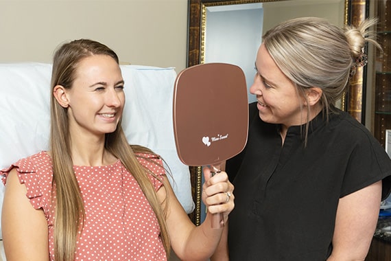 A MedSpa specialist and patient looking in the mirror and smiling after procedure results